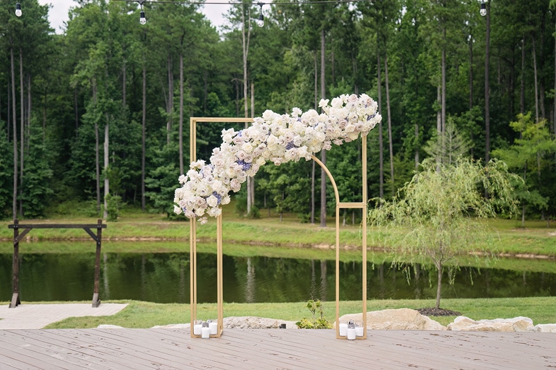 A Pinehill Pavilion Wedding arch decorated with flowers in front of a pond.
