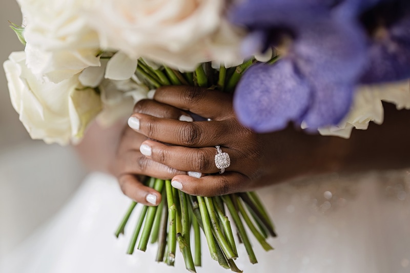 At the Pinehill Pavilion Wedding, a bride's hand delicately holds a breathtaking bouquet of purple and white flowers.
