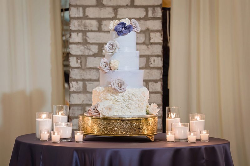 A Pinehill Pavilion wedding cake on a table with candles.