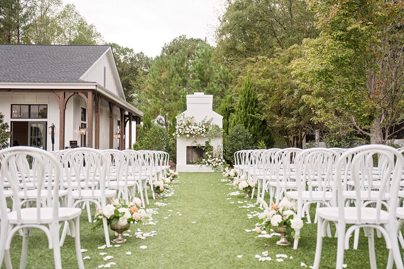 An outdoor wedding ceremony at The Bradford wedding venue with white chairs and a fireplace.