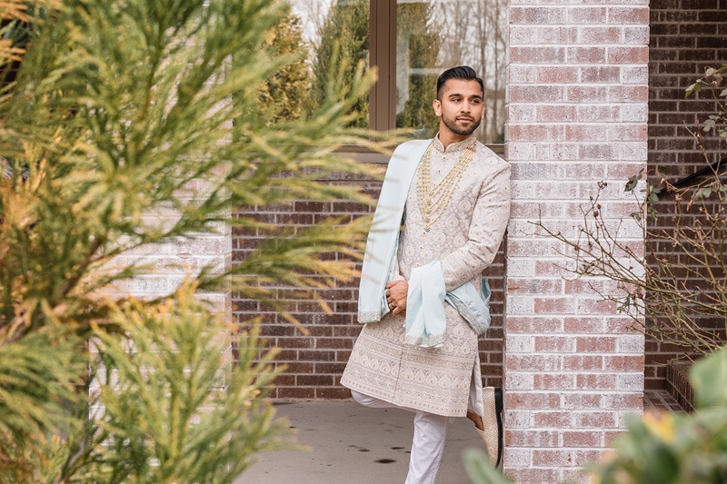 An Indian groom posing at The Bradford Wedding venue in front of a brick wall.