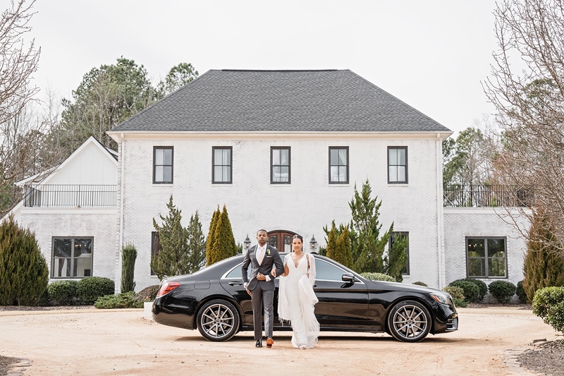 The bride and groom are posing next to a black Mercedes Benz at The Bradford Wedding Venue.