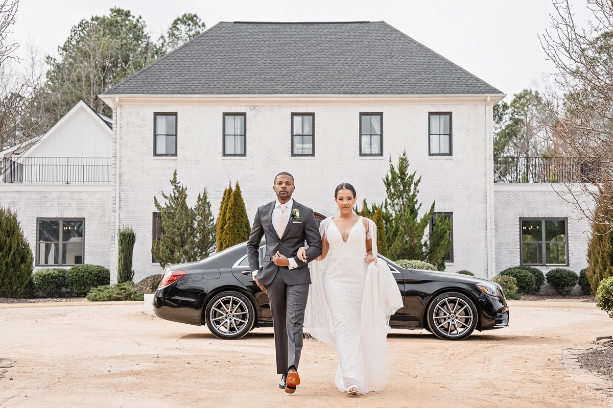 A bride and groom walk in front of a black Mercedes Benz at The Bradford Wedding Venue.