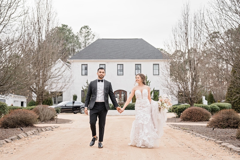 A bride and groom walking down a dirt road in front of The Bradford wedding venue.
