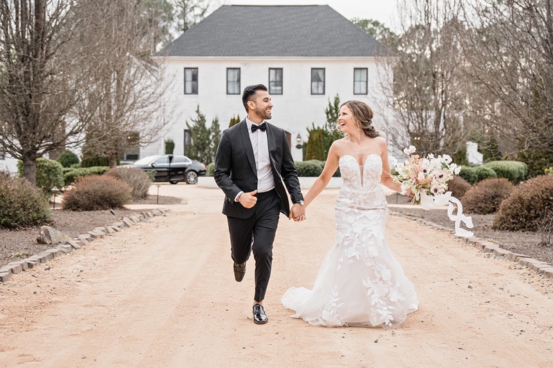 A bride and groom walking down a dirt road in front of The Bradford Wedding Venue.