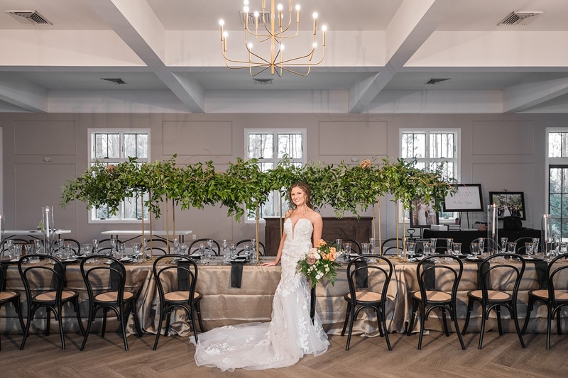 A woman in a white dress stands in front of a long table and chairs at The Bradford Wedding Venue.