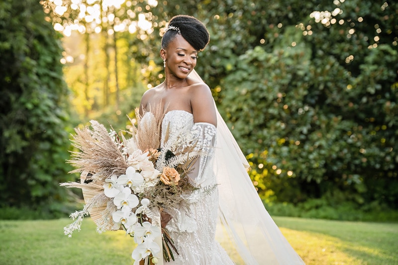 A bride at "the distillery wedding" holding a bouquet in a grassy field.