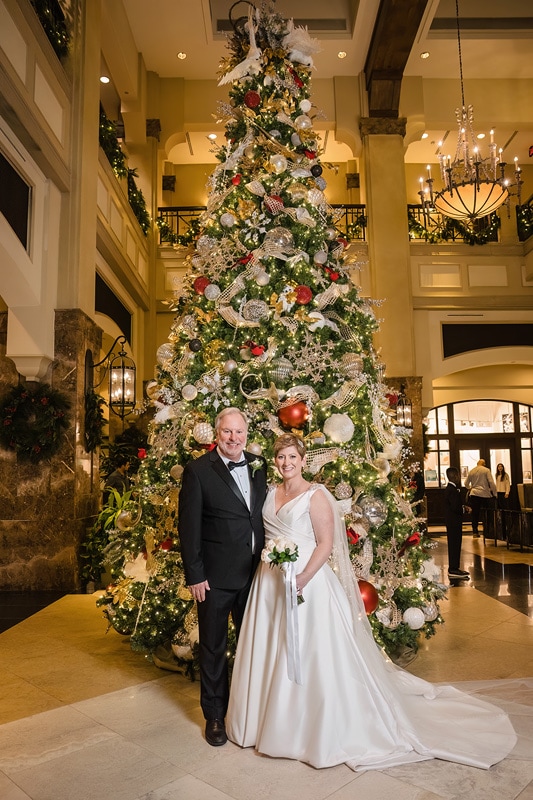 A bride and groom standing in front of a Christmas tree at their Grandover Resort & Spa Wedding Reception.