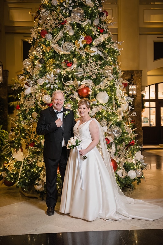 A man and woman posing for a picture in front of a Christmas tree at their Westminster Presbyterian Church wedding.