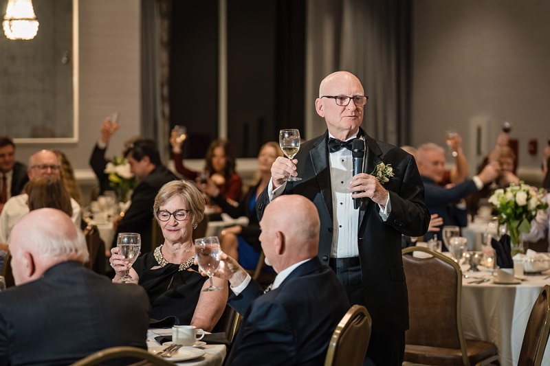 A man in a tuxedo is giving a toast at a wedding banquet.