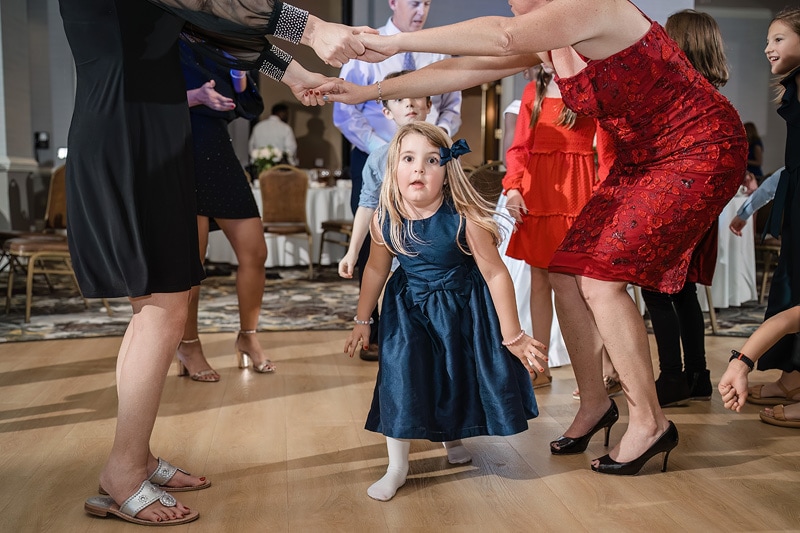 A group of people holding hands and a little girl in a blue dress at a Grandover Resort & Spa wedding reception.