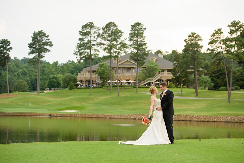 A man and woman in wedding attire standing on grass near water at a Governors Club Wedding.