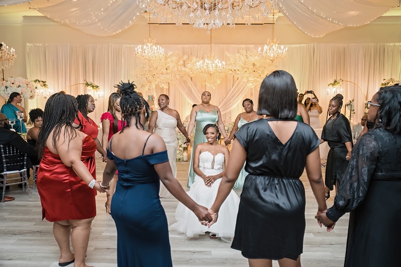 A bride and groom hold hands and dance joyfully in the center of a circle formed by elegantly dressed guests at the Crystal Ballroom in Charlotte.