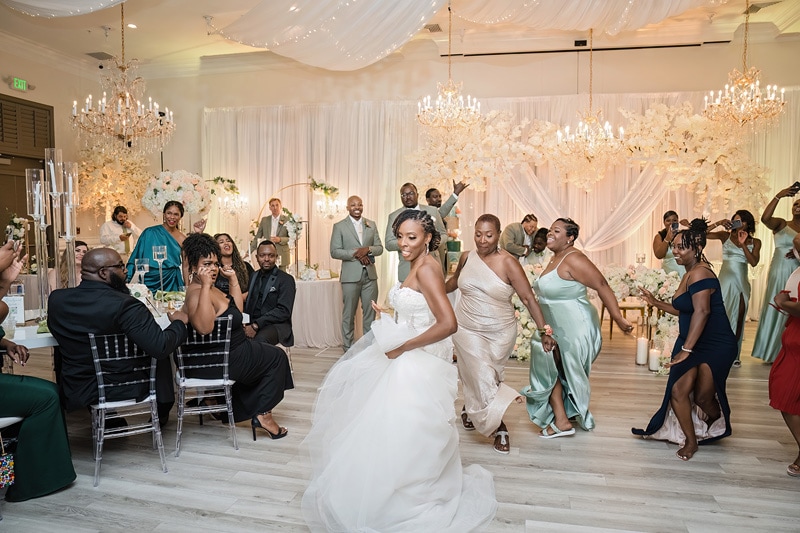 A bride joyfully tosses her bouquet towards a group of expectant women at a Crystal Ballroom Charlotte wedding reception, while guests observe the tradition with smiles and anticipation.
