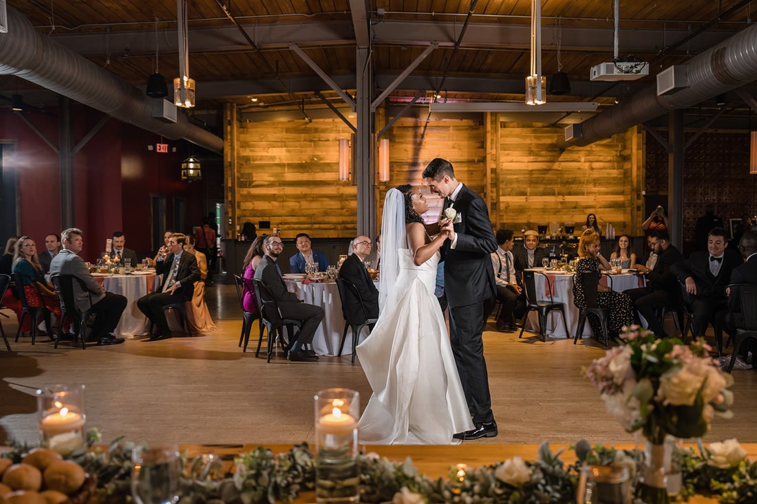 A newlywed couple shares their first dance at The Rickhouse, surrounded by guests and candlelit tables, embodying an intimate and joyful wedding reception moment.