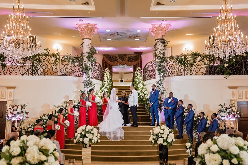 A wedding ceremony taking place in the grand marquise ballroom with guests seated on either side as the bridal party stands at the altar.