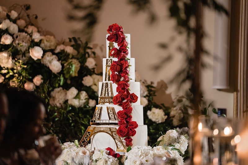 A multi-tiered wedding cake with an Eiffel Tower design and red roses, displayed at the grand marquise ballroom.