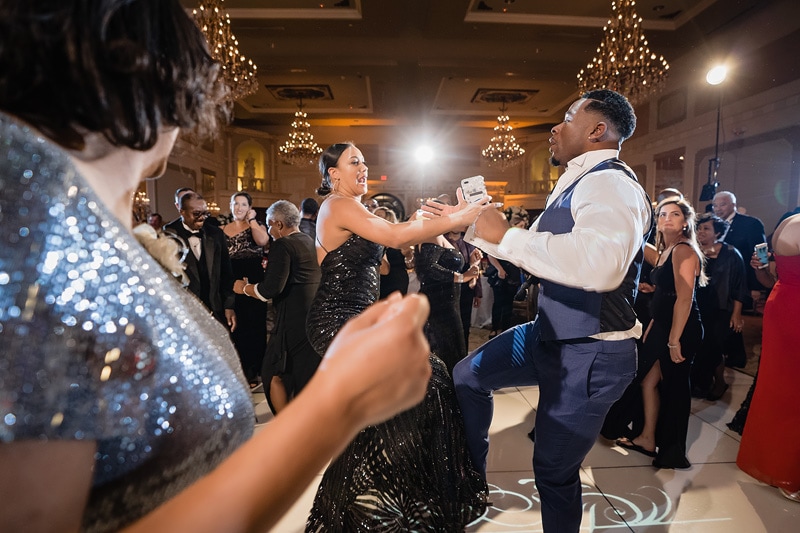 A couple dances enthusiastically at a grand marquise ballroom wedding with other attendees in the background.
