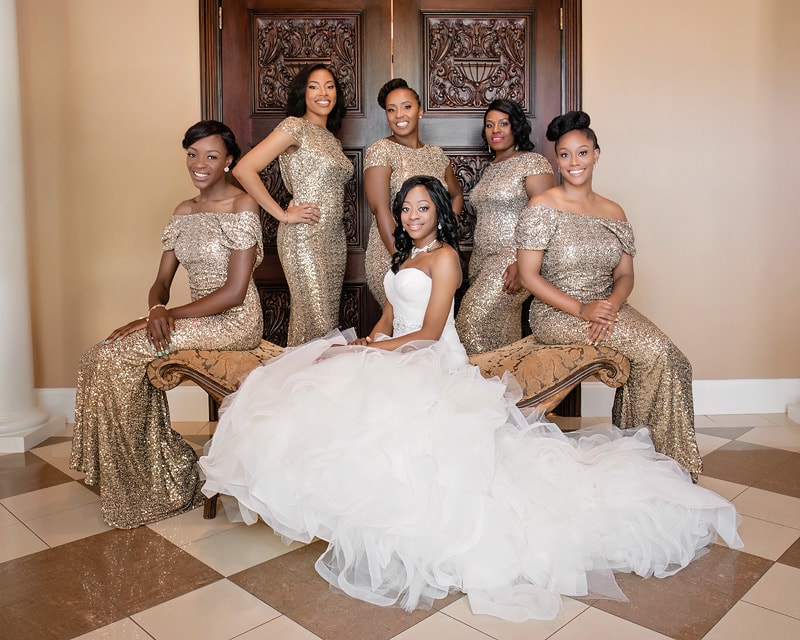 A bride in a white gown sits surrounded by her bridesmaids wearing matching golden dresses at the Grand Marquise Ballroom.