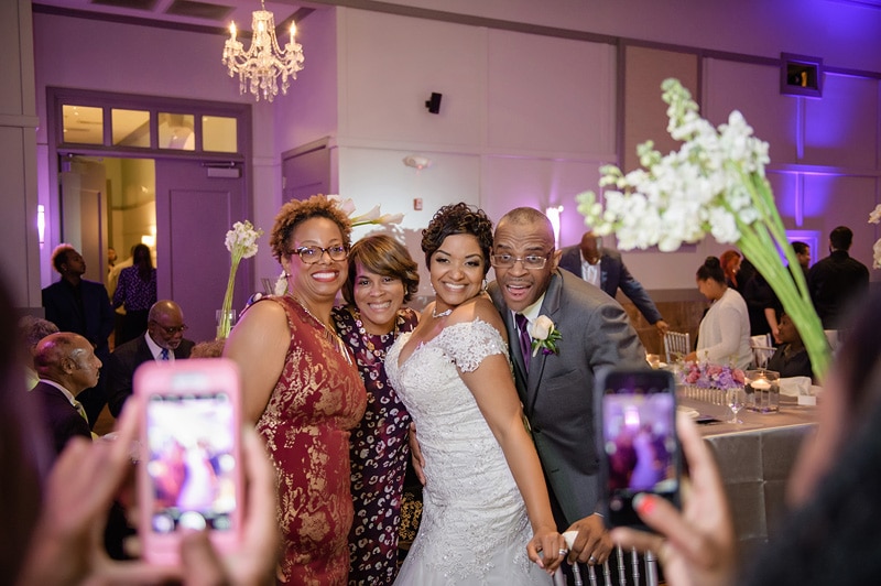 A joyful bride poses for photos with her family at a Paramount Event Venue wedding, the group sharing a moment of laughter and celebration, with guests and elegant decor in the background.