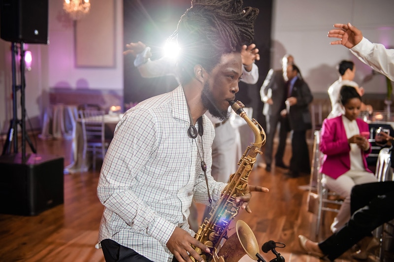 A dynamic saxophonist plays with intense focus at a Paramount Event Venue wedding, where guests in the background enjoy the ambiance with dancing and socializing.