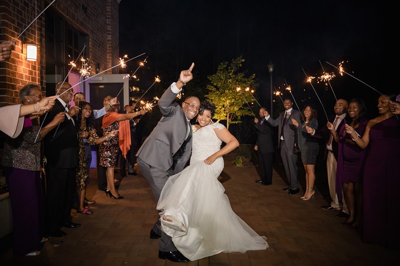 A joyful newlywed couple make a triumphant exit through a sparkling lineup of friends and family at the Paramount Event Venue, celebrating with jubilant cheers and raised sparklers.