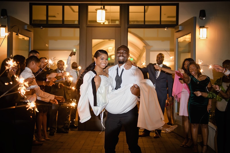 A joyous couple makes their wedding exit through a sparkling tunnel of friends and family holding sparklers at the Paramount Event Venue, capturing a moment of blissful celebration.