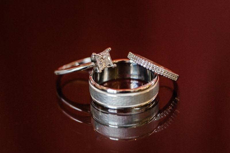 A pair of elegant wedding rings, one with a prominent diamond and the other with pavé-set stones, resting atop a polished, reflective surface at the Paramount Event Venue, symbolizing love and commitment.