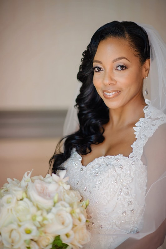 A radiant bride in a lace-detailed gown smiles gently while holding a bouquet of white flowers, her happiness captured in a soft-focus portrait at the Paramount Event Venue wedding.