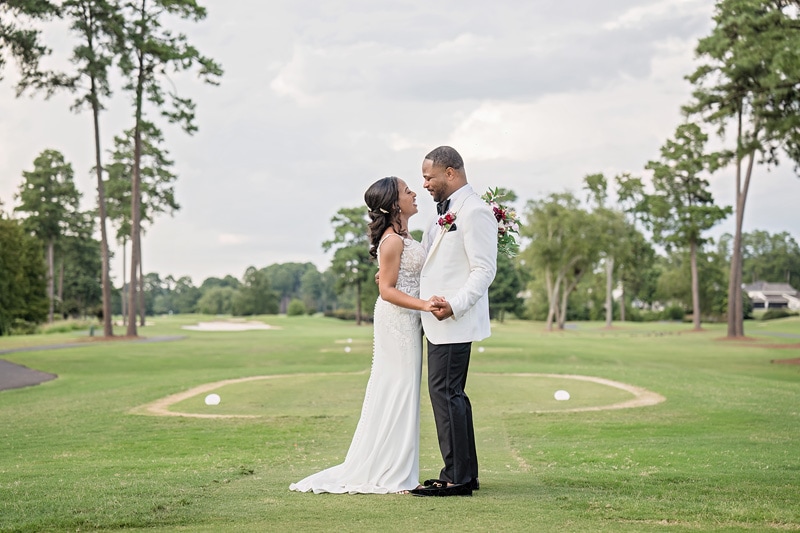 A couple dressed in wedding attire shares an intimate moment at Prestonwood Country Club, with lush greenery and gathering clouds above, symbolizing the beginning of their life's journey together.