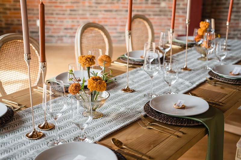 An elegantly set dining table with tall candles, crystal glassware, patterned textiles, and vibrant marigolds, ready for a sophisticated gathering at The Power House NC at Rocky Mount Mills.