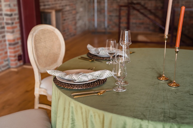 An elegant dining table set for a sophisticated meal at The Power House NC at Rocky Mount Mills Wedding Venue, featuring ornate plates, gleaming cutlery, crystal stemware, and tall candle holders