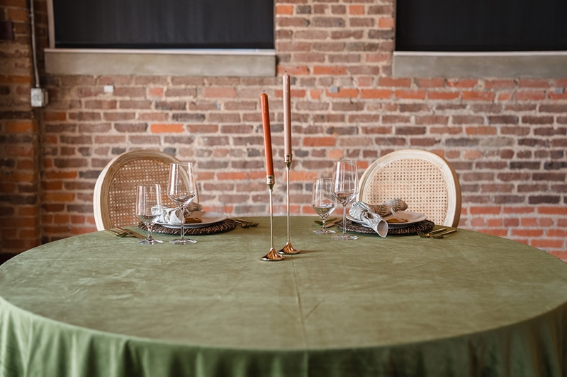 Elegant table setup at The Power House NC wedding venue with two place settings, featuring golden utensils, wine glasses, and a tall candle holder, against a rustic brick wall backdrop.