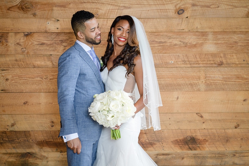 A radiant couple on their wedding day at The Rickhouse, sharing a joyful moment, with the bride in an elegant white gown and veil holding a bouquet, and the groom in a stylish gray suit,